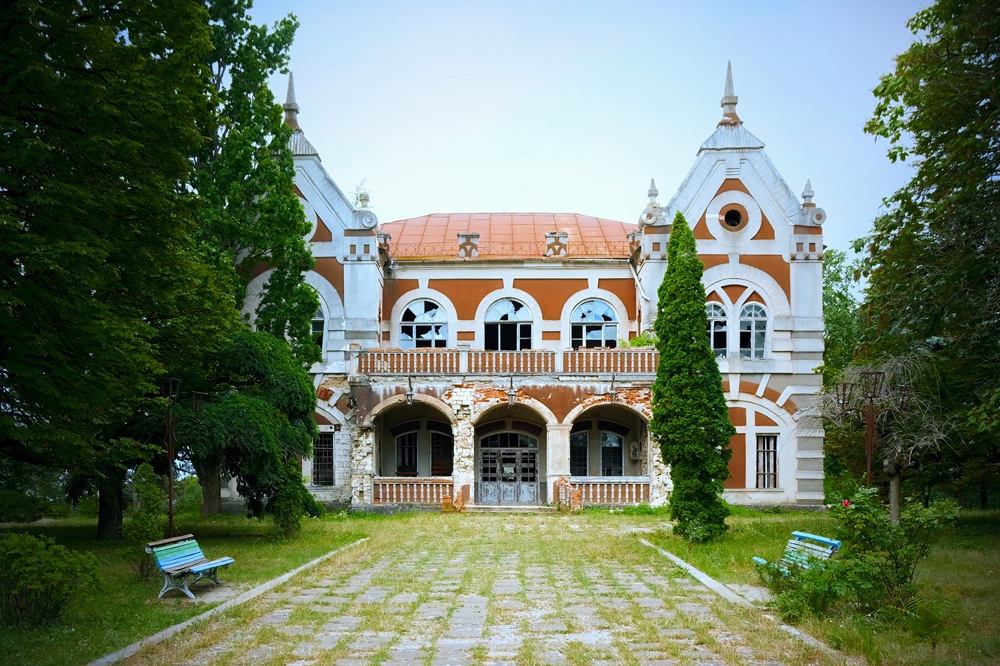 Abandoned old house with greenery, path and benches in front of it in Moldova